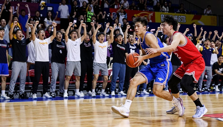 A dynamic scene featuring college basketball stars engaged in an intense game on a vibrant basketball court. In the foreground, two male players, one wearing a blue jersey and the other in red, are mid-play, displaying athleticism and concentration. Their expressions reflect determination as they compete for the ball. In the middle ground, teammates cheer enthusiastically, showing a mix of excitement and encouragement, dressed in casual college apparel. The background is filled with a cheering crowd, providing an atmosphere of energy and enthusiasm, with banners and team colors. The lighting highlights the players, casting dramatic shadows and creating depth. The camera angle is low, emphasizing the action and intensity of the game, capturing the essence of competitive college basketball.