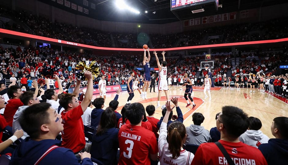 A vibrant college basketball arena packed with enthusiastic fans showcasing the intense atmosphere of a basketball rivalry. In the foreground, specify fans in team colors, wearing jerseys and face paint, displaying passionate expressions. The middle ground features players engaged in a dynamic play, one shooting a basket while defenders leap to block, all in a moment of high energy. In the background, a scoreboard displays a close game score, and cheerleaders rally the crowd with pom-poms. The arena is illuminated with bright spotlights, casting dramatic shadows. Capture a sense of excitement and rivalry, with an emphasis on camaraderie and team spirit. The angle should be slightly elevated, showcasing both the action on the court and the lively crowd. Aim for a colorful, electric mood, celebrating the passion of college basketball. A vibrant college basketball arena packed with enthusiastic fans showcasing the intense atmosphere of a basketball rivalry. In the foreground, specify fans in team colors, wearing jerseys and face paint, displaying passionate expressions. The middle ground features players engaged in a dynamic play, one shooting a basket while defenders leap to block, all in a moment of high energy. In the background, a scoreboard displays a close game score, and cheerleaders rally the crowd with pom-poms. The arena is illuminated with bright spotlights, casting dramatic shadows. Capture a sense of excitement and rivalry, with an emphasis on camaraderie and team spirit. The angle should be slightly elevated, showcasing both the action on the court and the lively crowd. Aim for a colorful, electric mood, celebrating the passion of college basketball.