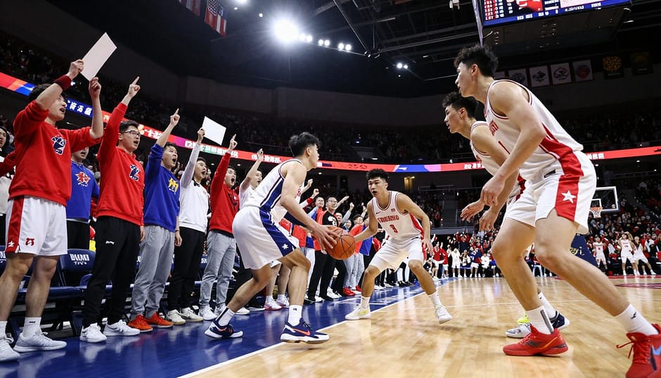 A dynamic college basketball rivalry scene set in a packed arena, showcasing two rival teams in vibrant jerseys. In the foreground, a diverse group of male and female fans, wearing their team colors, passionately cheering and holding signs, embodying the energy of rivalry. The middle ground features players locked in an intense game moment, a point guard dribbling while a defender pressures closely. The background reveals the arena's scoreboard and cheering crowd, illuminated by dramatic stadium lights for a high-energy atmosphere. The angle captures the action from a low perspective, emphasizing the intensity of competition and camaraderie. The overall mood is electric and competitive, encapsulating the spirit of college basketball rivalries in a safe and engaging way. A dynamic college basketball rivalry scene set in a packed arena, showcasing two rival teams in vibrant jerseys. In the foreground, a diverse group of male and female fans, wearing their team colors, passionately cheering and holding signs, embodying the energy of rivalry. The middle ground features players locked in an intense game moment, a point guard dribbling while a defender pressures closely. The background reveals the arena's scoreboard and cheering crowd, illuminated by dramatic stadium lights for a high-energy atmosphere. The angle captures the action from a low perspective, emphasizing the intensity of competition and camaraderie. The overall mood is electric and competitive, encapsulating the spirit of college basketball rivalries in a safe and engaging way.