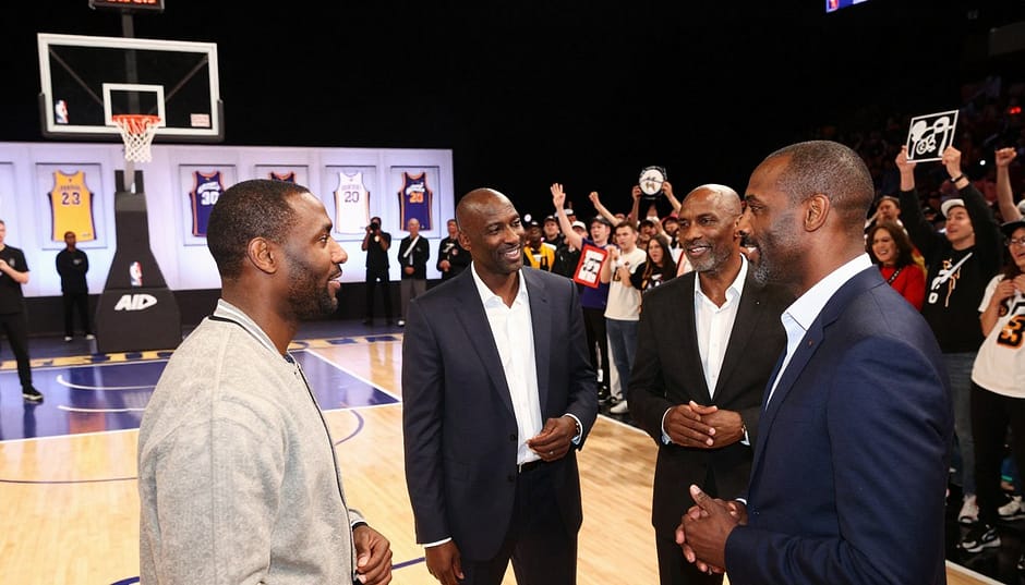 A dynamic composition of former NBA players gathered at a professional event celebrating their careers. In the foreground, a group of three former players, dressed in smart casual attire, engage in conversation, their expressions lively and animated. The middle layer features a brightly lit stage with a basketball hoop and jerseys displayed, symbolizing their journey in the sport. In the background, a cheering crowd wearing Jazz colors, filled with energetic fans holding memorabilia, enhances the atmosphere of excitement and nostalgia. The scene is captured with a slightly elevated angle, using soft, warm lighting to evoke a celebratory mood, highlighting the camaraderie and passion these players have for the game. A dynamic composition of former NBA players gathered at a professional event celebrating their careers. In the foreground, a group of three former players, dressed in smart casual attire, engage in conversation, their expressions lively and animated. The middle layer features a brightly lit stage with a basketball hoop and jerseys displayed, symbolizing their journey in the sport. In the background, a cheering crowd wearing Jazz colors, filled with energetic fans holding memorabilia, enhances the atmosphere of excitement and nostalgia. The scene is captured with a slightly elevated angle, using soft, warm lighting to evoke a celebratory mood, highlighting the camaraderie and passion these players have for the game.